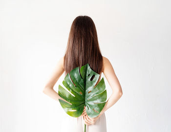 Rear view of woman holding leaf standing against white background