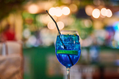 Blue lagoon cocktail in glass with straw, night cafe light bokeh background. blue cocktail drink