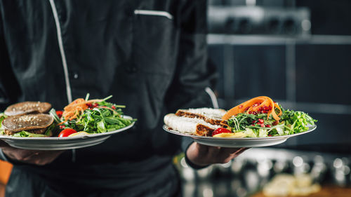 Midsection of chef holding food in plates at restaurant