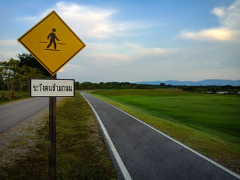 Information sign on road by field against sky