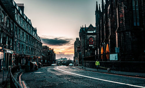 Road amidst buildings against sky during sunset