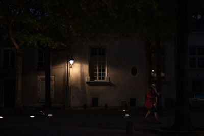 Woman walking on illuminated street amidst buildings at night