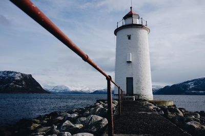 Lighthouse on calm lake in front of mountains against sky