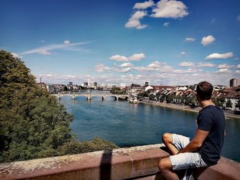 Side view of man sitting on retaining wall against sky