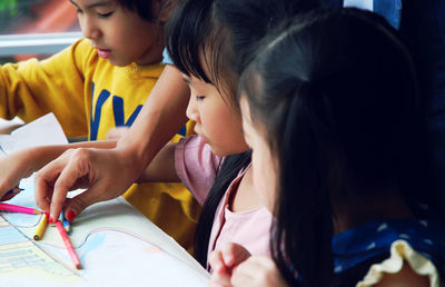 Cropped hand of teacher giving colored pencils to children drawing on paper