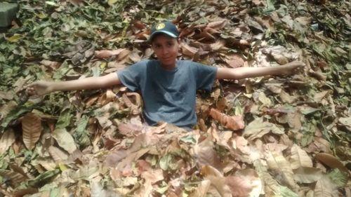 Portrait of young man with arms outstretched leaves