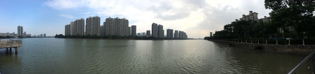 Panoramic view of city skyline by river against sky