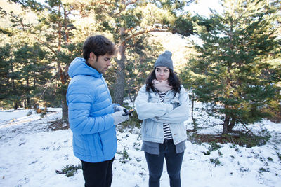 Man using mobile phone by angry woman while standing on snow covered field