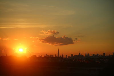 Silhouette of city against cloudy sky during sunset