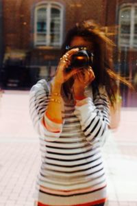 Portrait of young woman photographing with city in background