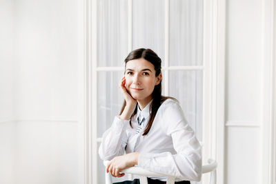 Portrait of young woman standing against white wall