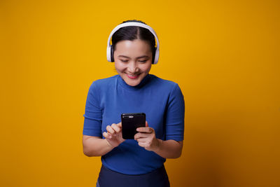 Young man using mobile phone against yellow background