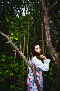 Portrait of woman standing by tree in forest