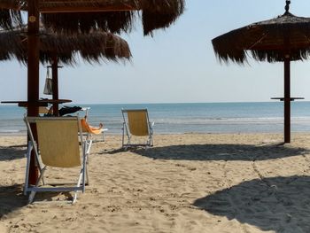 Chairs on beach by sea against clear sky