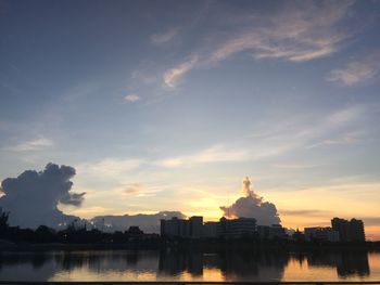 Buildings by river against sky during sunset