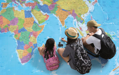 High angle view of tourists with backpacks sitting on map