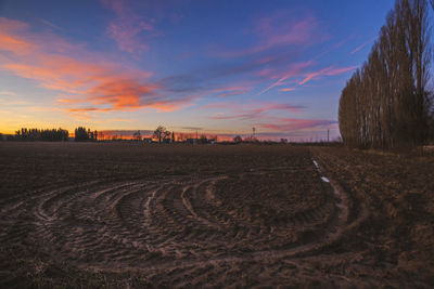 Tire tracks on farm against sky at sunset