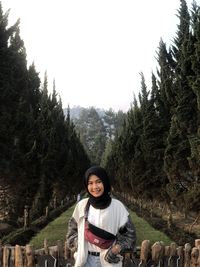 Portrait of smiling young woman standing against trees