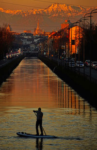 Rear view of silhouette man on river at sunset