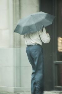 Low section of man with umbrella walking in rain