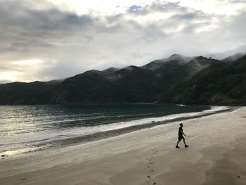 Man walking at beach against mountains during sunset