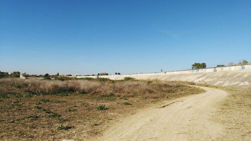 Road amidst field against clear blue sky