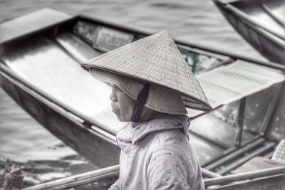 Side view of mature woman wearing asian style conical hat sitting in boat on lake