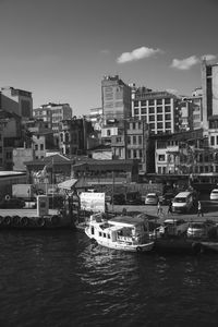 Boats in river by buildings in city against sky