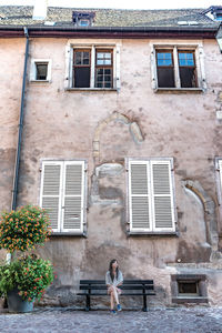 Woman sitting on bench against building