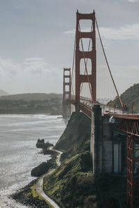 Suspension bridge over river against cloudy sky