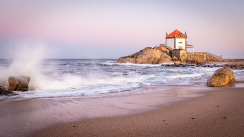 Lighthouse on beach by sea against sky