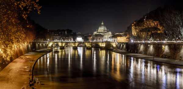 Bridge over river by illuminated buildings at night