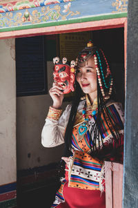 Young woman holding camera while standing against the wall
