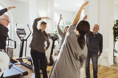 Female caregiver assisting elderly men and women to exercise at nursing home