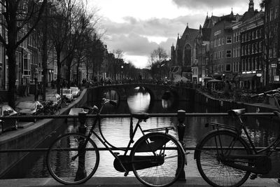 Bicycle parked on bridge over canal amidst buildings in city