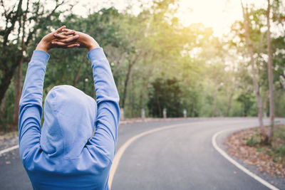 Woman exercising on road amidst trees