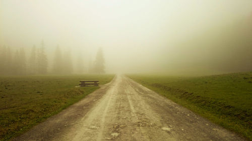 Country road amidst field against sky during foggy weather