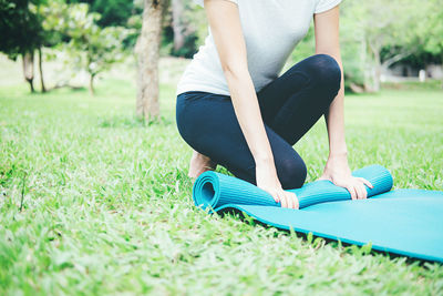 Low section of woman rolling exercise mat on grassy field at park