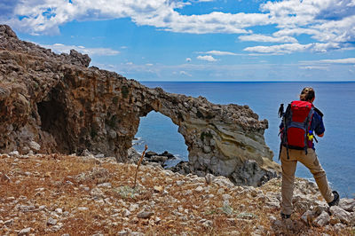 Rear view of man standing on rock by sea against sky