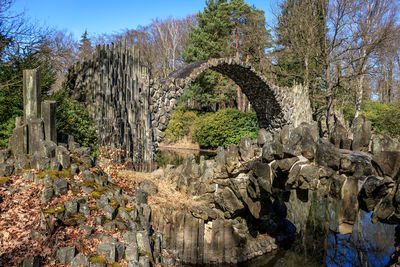 Trees growing by arch bridge against sky