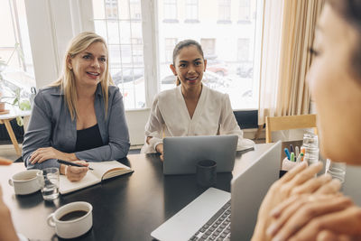 Smiling female entrepreneurs sitting at table during business meeting in office