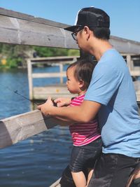 Side view of father and toddler daughter fishing at lake