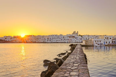 Scenic view of river by buildings against sky during sunset