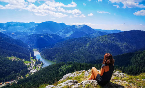Woman sitting on mountain looking at mountains against sky
