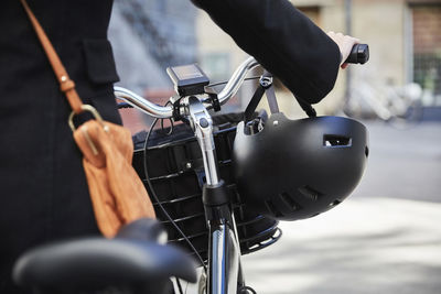 Midsection of woman walking with electric bicycle in city