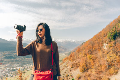 Woman photographing at camera against sky