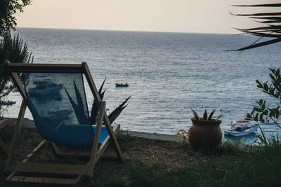 Chairs on shore by sea against sky