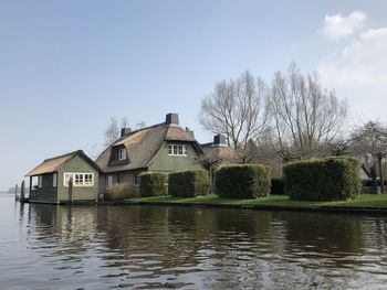 House by lake and buildings against sky