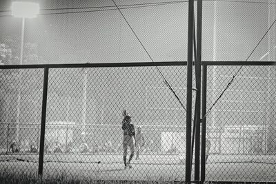 Rear view of man standing by chainlink fence