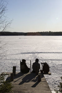 Rear view of boys sitting on jetty over frozen lake during sunny day